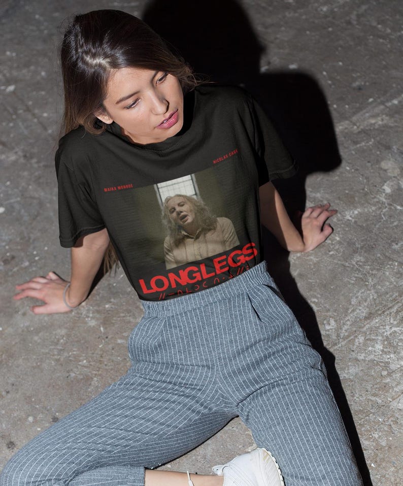 Puede incluir: Una camiseta negra con un estampado gr&aacute;fico de una mujer con el texto "LONGLESS" en rojo. La mujer lleva una camisa marr&oacute;n claro y tiene el pelo rubio. El texto "KILLA BEAST" est&aacute; en blanco en la parte superior del gr&aacute;fico. El texto "WICKED GAME" est&aacute; en blanco en la parte inferior del gr&aacute;fico.