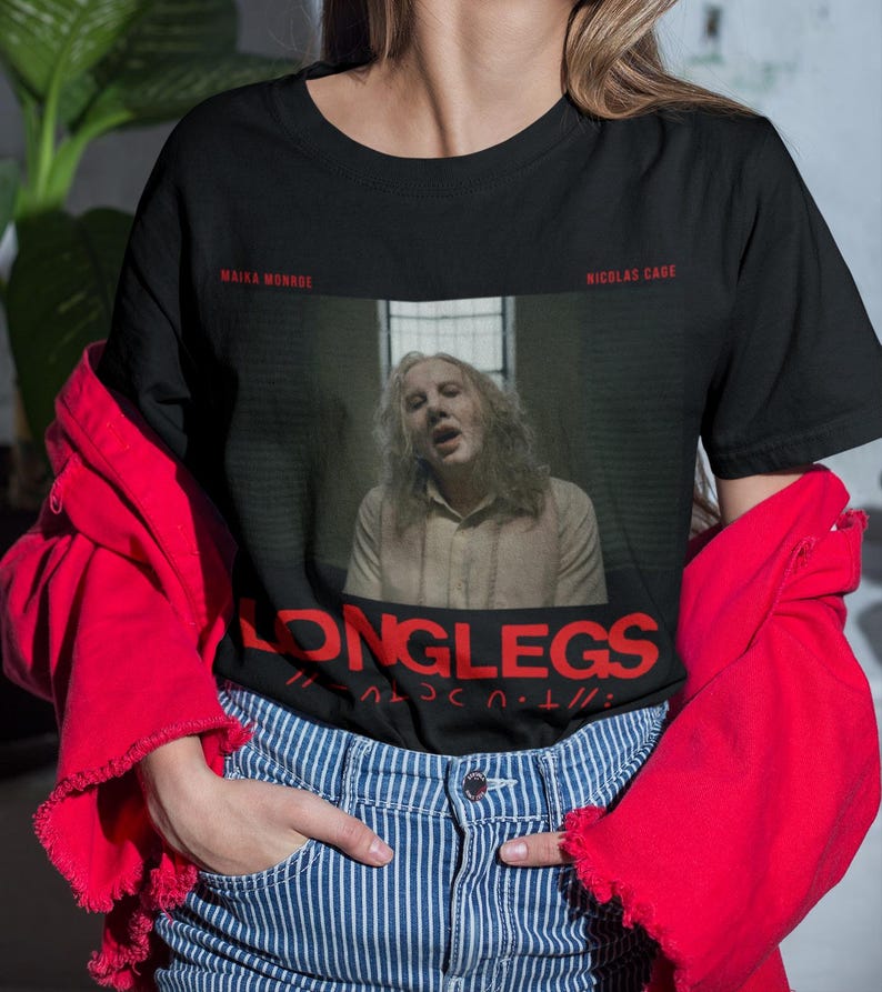 Puede incluir: Camiseta negra con un gr&aacute;fico de Nicolas Cage de la pel&iacute;cula "Longlegs". El gr&aacute;fico est&aacute; en un estilo de foto en blanco y negro con el t&iacute;tulo "Longlegs" en texto rojo.