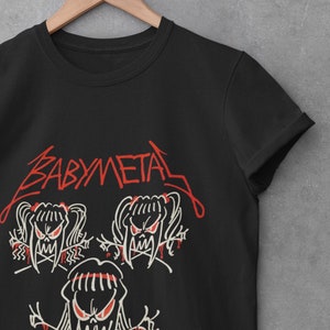 Pode incluir: Camiseta preta com um logotipo "BABYMETAL" vermelho e uma imagem de desenho animado branca de tr&ecirc;s meninas com presas e rabos de cavalo.