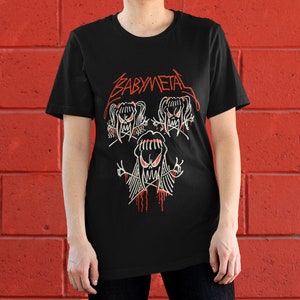 Pode incluir: Camiseta preta com um logotipo "BABYMETAL" vermelho e um gr&aacute;fico de tr&ecirc;s figuras de desenhos animados com olhos e bocas vermelhos.