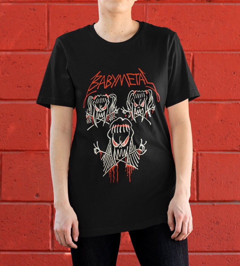 Pode incluir: Camiseta preta com um logotipo "BABYMETAL" vermelho e um gr&aacute;fico de tr&ecirc;s figuras de desenhos animados com olhos e bocas vermelhos.