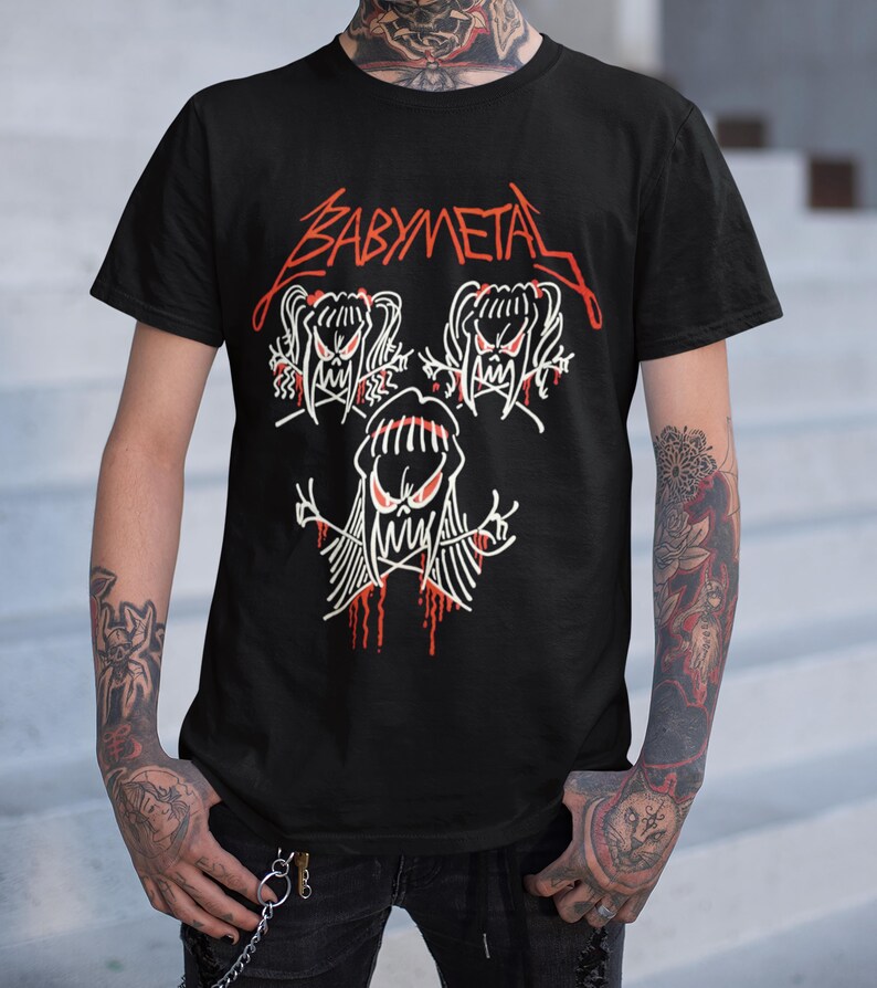 Pode incluir: Camiseta preta com um gr&aacute;fico branco de tr&ecirc;s figuras de desenhos animados com o texto "BABYMETAL" em vermelho acima.