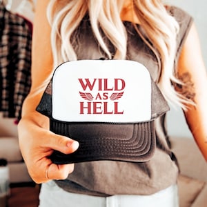 May include: A white and black trucker hat with the text "WILD AS HELL" in red lettering and red wings on either side of the text.
