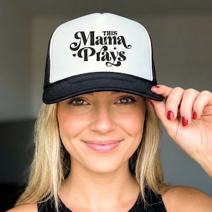 May include: A black and white trucker hat with the text "This Mama Plays" in a stylish font. The hat has a white front panel and a black mesh back. The brim is black.