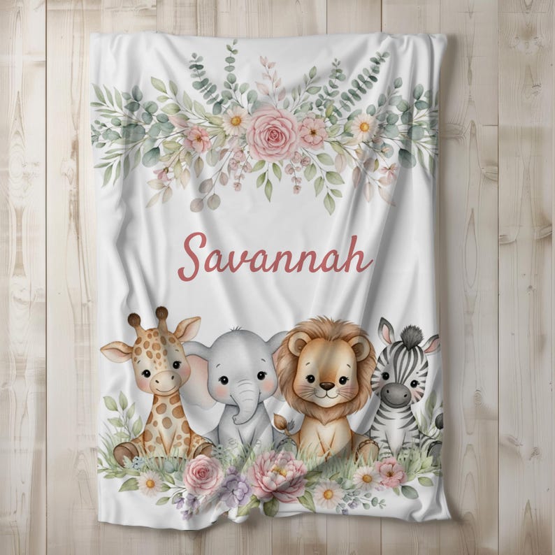 May include: White baby blanket featuring a floral design with pink roses and greenery. The blanket has the name "Savannah" in pink script, and illustrations of a giraffe, elephant, lion, and zebra.