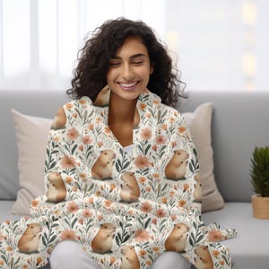 May include: A white throw blanket with a floral pattern featuring small brown and white guinea pigs. The blanket is made of soft, cosy fabric and is perfect for snuggling up on the sofa.