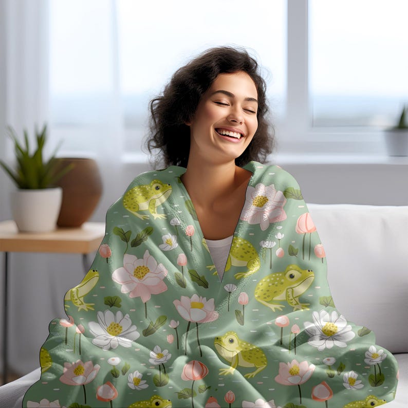 May include: A green fleece blanket with a pattern of frogs, pink and white flowers, and green leaves. A person is wrapped in the blanket.