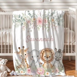 May include: White baby blanket with the name "Savannah" in pink script. The blanket features a floral design with pink roses and green leaves. Below the name are illustrations of a giraffe, elephant, lion, and zebra.