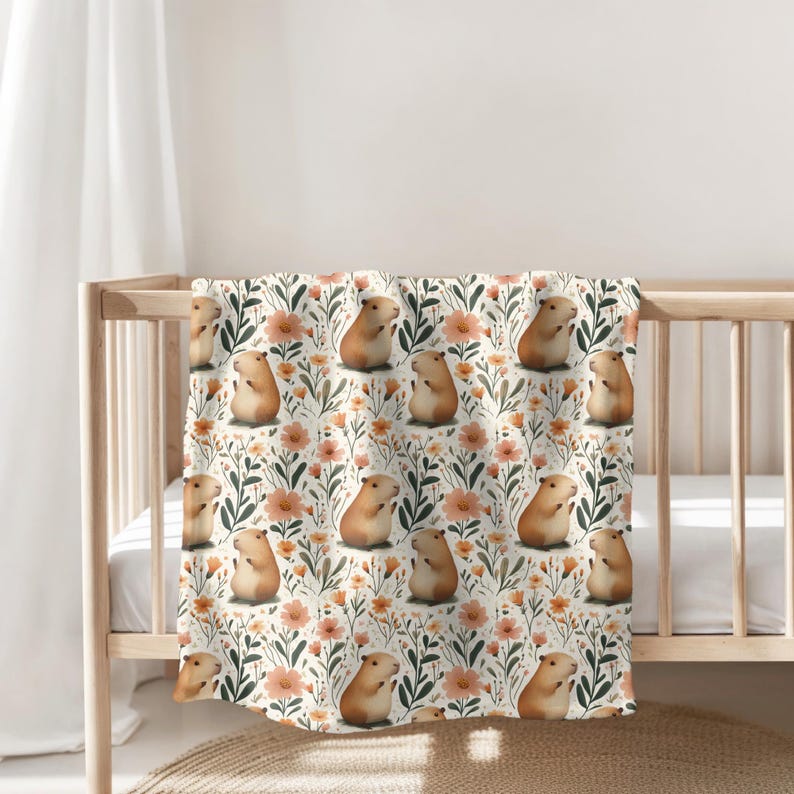 May include: A white baby blanket with a repeating pattern of brown guinea pigs and orange flowers. The guinea pigs are sitting up and looking to the right.