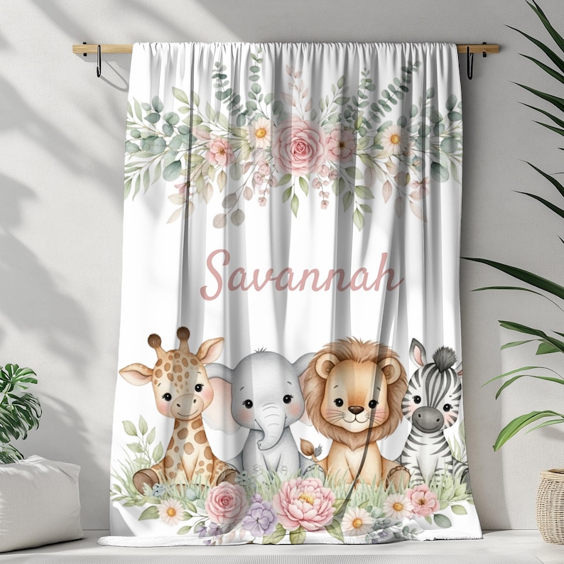 May include: White curtain with a floral and foliage design at the top, featuring the name "Savannah" in pink script. Below, are illustrations of a giraffe, elephant, lion, and zebra. The curtain is decorated with flowers and greenery.