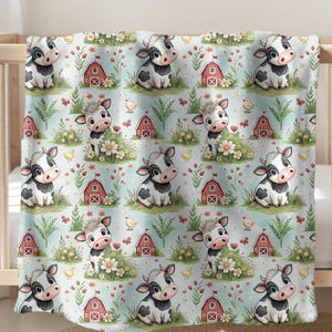 May include: A baby blanket with a repeating pattern of cartoon cows, red barns, flowers, and butterflies on a light blue background. The blanket is draped over a wooden crib.