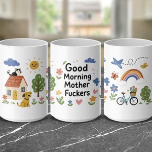 May include: A white ceramic mug featuring a colorful illustration of a house, a cat, a dog, a sun, a bicycle, a rainbow, and flowers. The text Good Morning Mother Fuckers is printed in black on the center of the mug with various small icons.