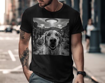 May include: A black and white t-shirt with a graphic of a golden retriever dog looking up at three flying saucers in the desert.