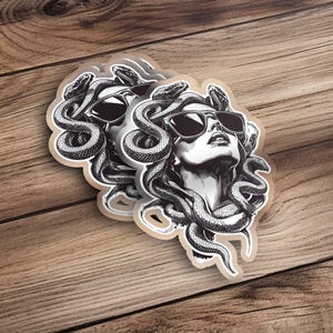 Könnte beinhalten: Ein schwarz-weißer Aufkleber mit einer Frau mit Schlangenhaaren, die eine Sonnenbrille trägt. Das Gesicht der Frau schaut nach oben und ihre Haare sind so gestylt, dass sie einer Krone ähneln.