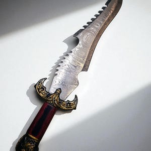 May include: An ornate dagger with a patterned steel blade and a serrated edge. The handle is red and black with gold-colored decorative elements. The dagger is approximately 18 inches long.