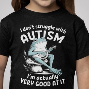 May include: Black t-shirt with a white frog playing a banjo on a mushroom. The text on the shirt reads "I don't struggle with AUTISM I'm actually VERY GOOD AT IT."