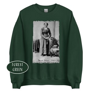 May include: Forest green sweatshirt featuring a black and white image of Harriet Tubman. The image is framed with a white border and includes the text "Harriet Tubman (1822-1913) nurse, spy and scout."