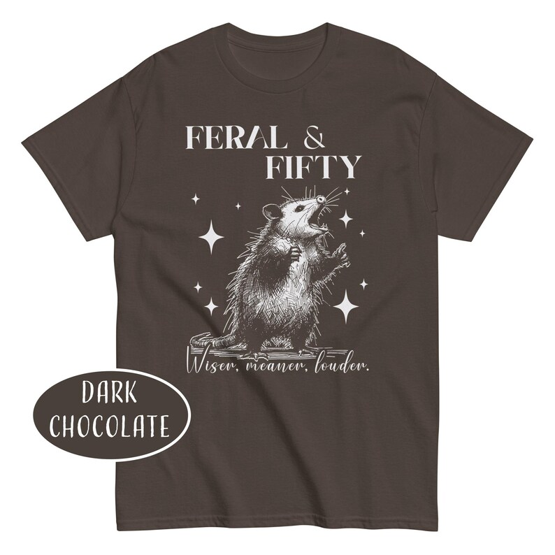 May include: Dark chocolate brown t-shirt with a graphic of an opossum and the text "FERAL & FIFTY". The opossum is drawn in black and white with its mouth open. The shirt also has the text "Wiser, meaner, louder."