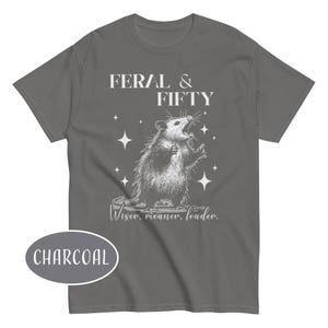 May include: Charcoal gray t-shirt with a graphic of an opossum with the text "FERAL & FIFTY" above it. Below the opossum is the text "Wiser, meaner, louder."