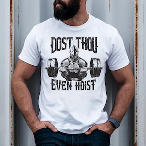 Pode incluir: Camiseta branca com um gráfico preto de um cavaleiro levantando uma barra. O texto "DOST THOU EVEN HOIST" está impresso acima e abaixo do cavaleiro. A camiseta tem gola redonda.