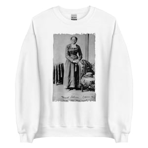 May include: White sweatshirt featuring a black and white image of Harriet Tubman. The image is a portrait of Tubman in a long dress, with text below reading "Harriet Tubman (1822-1913) nurse, spy and scout."