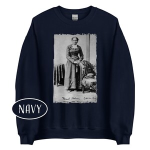 May include: Navy blue sweatshirt featuring a black and white image of Harriet Tubman. The image includes text that reads "Harriet Tubman (1823-1913) nurse, spy and scout." A white oval with the word "NAVY" is at the bottom.