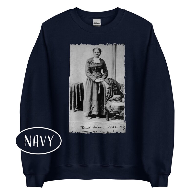 May include: Navy blue sweatshirt featuring a black and white image of Harriet Tubman. The image includes text that reads "Harriet Tubman (1823-1913) nurse, spy and scout." A white oval with the word "NAVY" is at the bottom.