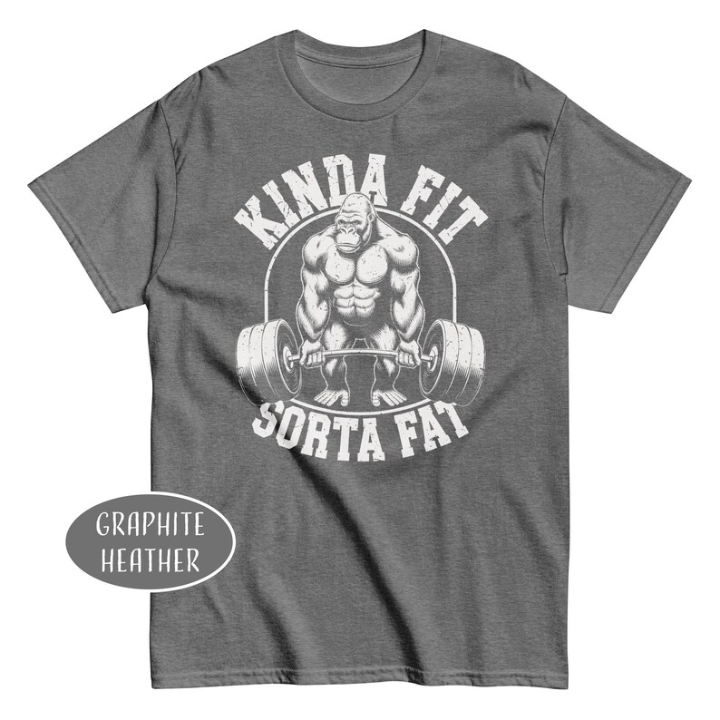 May include: Graphite heather t-shirt with a graphic of a gorilla lifting weights, encircled by the words "KINDA FIT" above and "SORTA FAT" below. The shirt is a dark gray color.