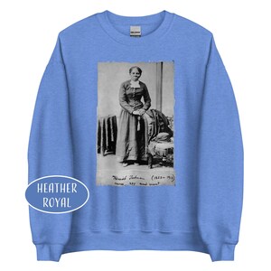 May include: Heather royal blue sweatshirt featuring a black and white image of Harriet Tubman. The image includes text that reads "Harriet Tubman (1822-1913) nurse, spy, and scout." A white oval with the words "Heather Royal" is on the bottom left.