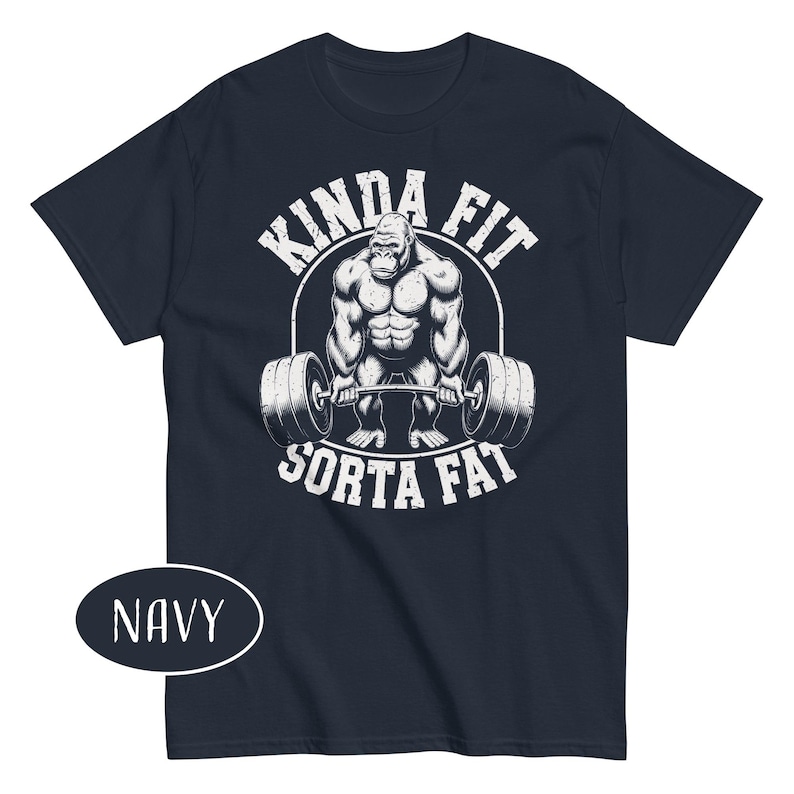 May include: Navy blue t-shirt with a white graphic of a gorilla lifting weights. The text "KINDA FIT" arches above the gorilla, and "SORTA FAT" is below. The shirt is a short-sleeved crew neck.