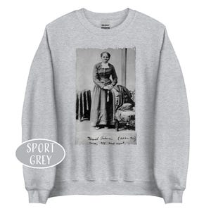 May include: Sport grey sweatshirt featuring a black and white image of Harriet Tubman. The image includes text that reads "Harriet Tubman (1822-1913) nurse, spy, and scout."