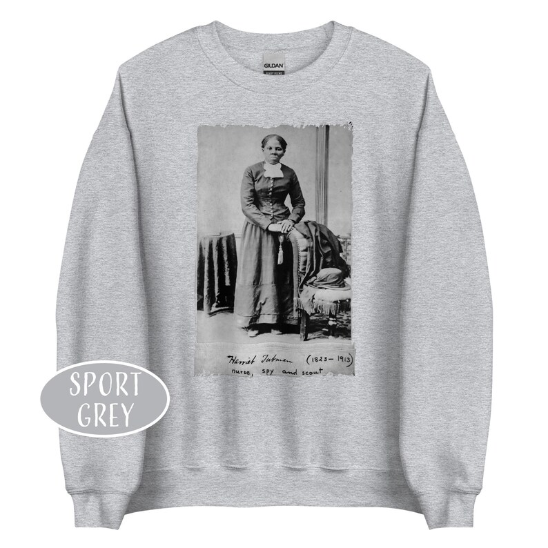 May include: Sport grey sweatshirt featuring a black and white image of Harriet Tubman. The image includes text that reads "Harriet Tubman (1822-1913) nurse, spy, and scout."