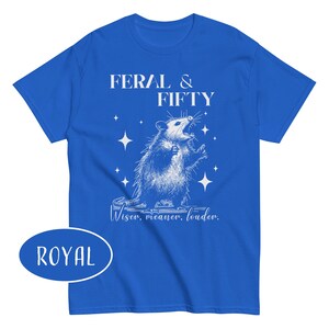 May include: Royal blue t-shirt with a white graphic of an opossum and the text "FERAL & FIFTY". Below the opossum is the text "Wiser, meaner, louder."