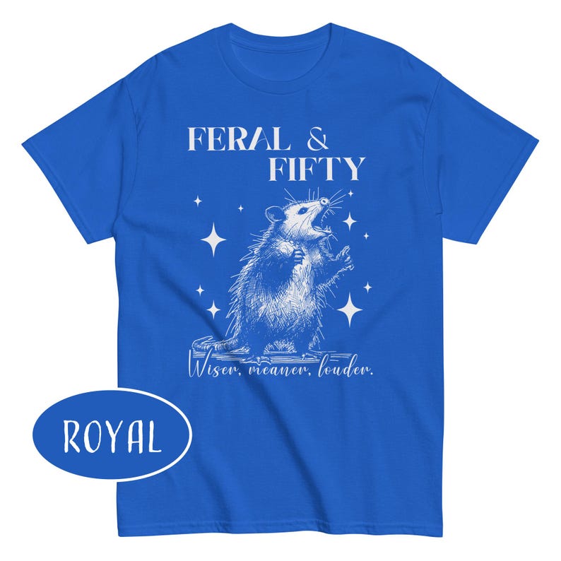 May include: Royal blue t-shirt with a white graphic of an opossum and the text "FERAL & FIFTY". Below the opossum is the text "Wiser, meaner, louder."