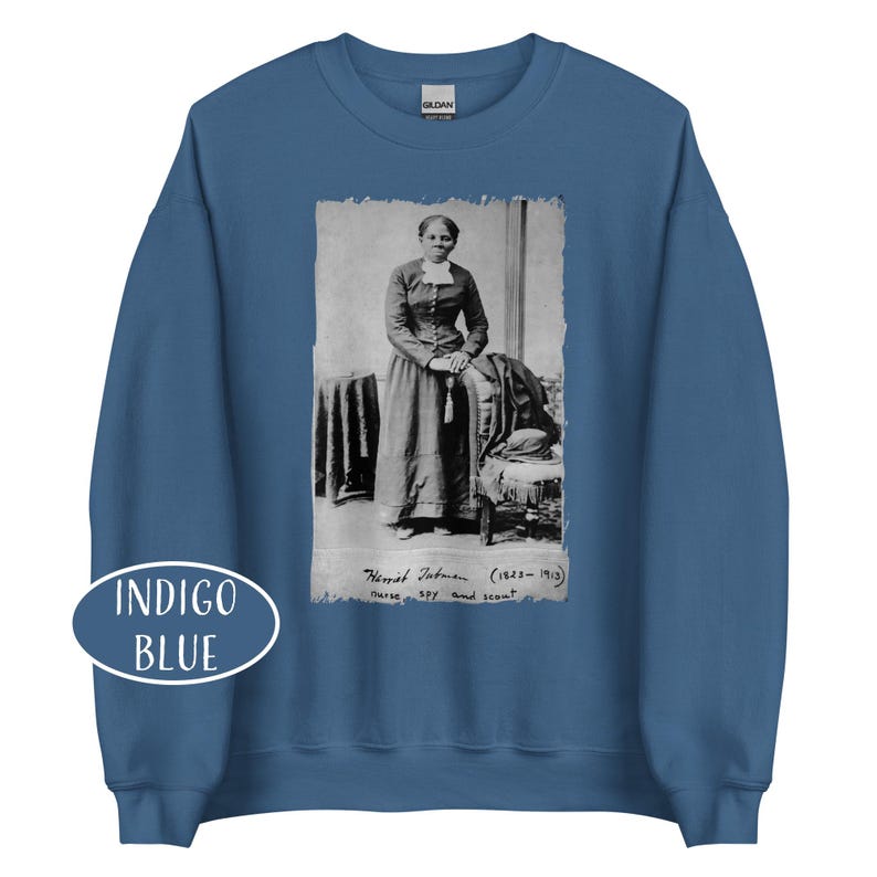 May include: Indigo blue sweatshirt featuring a black and white portrait of Harriet Tubman. The portrait includes the text "Harriet Tubman (1822-1913) nurse, spy, and scout". The sweatshirt has a crew neck and long sleeves.