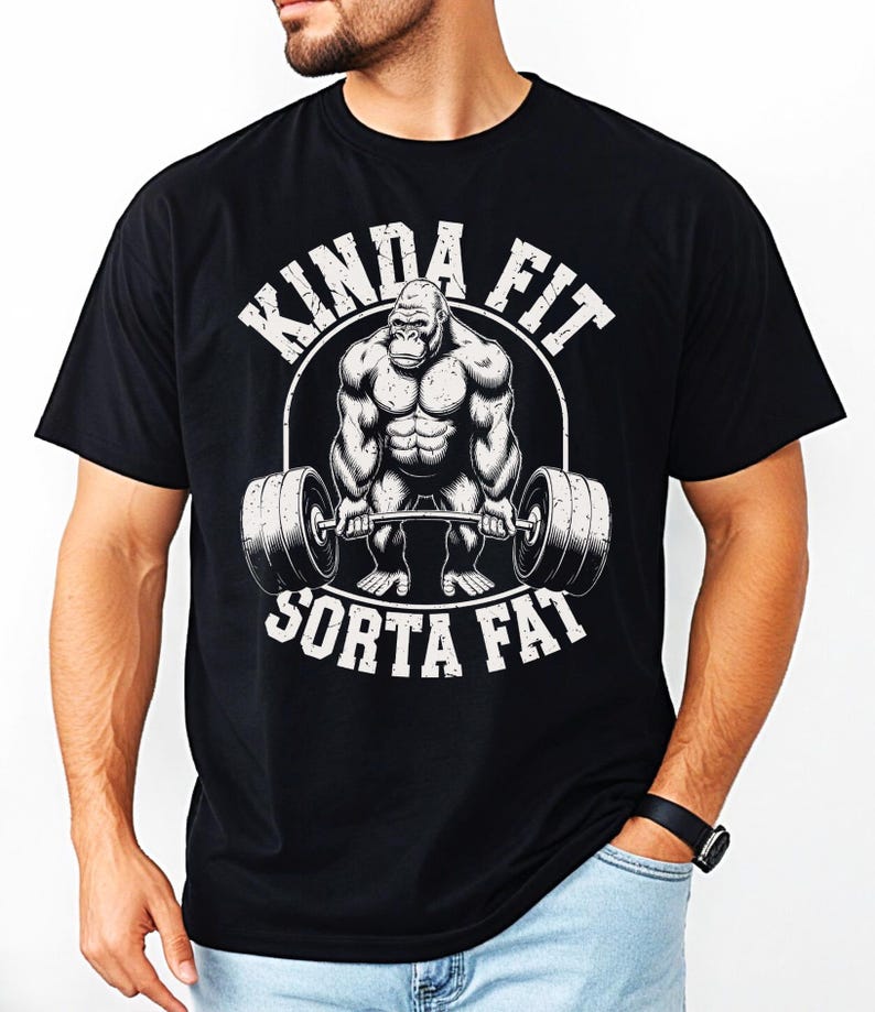 May include: Black t-shirt with a graphic of a muscular gorilla lifting a barbell. The text "KINDA FIT" arches above the gorilla, and "SORTA FAT" is below. The design is in white, creating a bold contrast against the black fabric.
