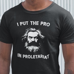 May include: Black t-shirt with white text that reads "I put the pro in proletariat" and a black and white illustration of Karl Marx.