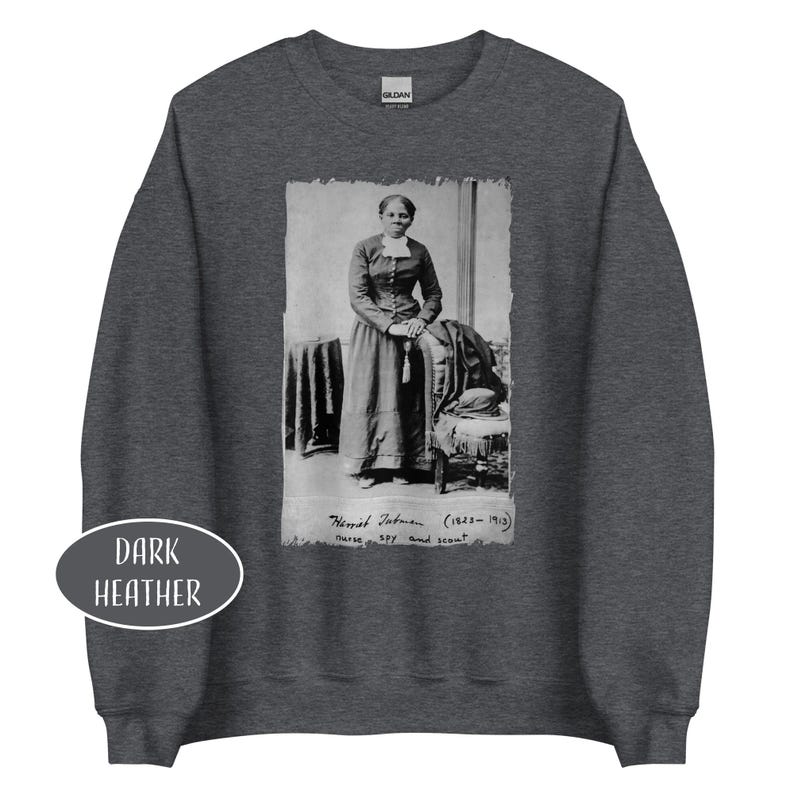 May include: Dark heather gray sweatshirt featuring a black and white image of Harriet Tubman. The image includes text that reads "Harriet Tubman (1823-1913) nurse, spy and scout."