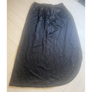 May include: A black, full-length skirt made of a shiny, silky material. The skirt has an elastic waistband and a scalloped hemline. The fabric drapes smoothly, creating a flowing silhouette. The skirt is suitable for various occasions.