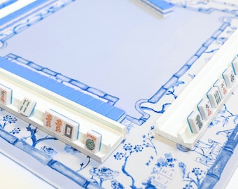 May include: A white mahjong set with blue tiles on a blue and white patterned table. The tiles are arranged in a traditional mahjong layout.