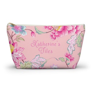 Könnte beinhalten: Kosmetiktasche mit rosafarbenem Blumendruck und Reißverschluss. Die Tasche trägt den Aufdruck "Katherine's Tiles".
