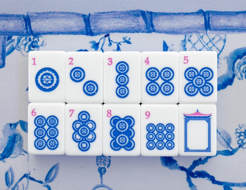 Puede incluir: Un juego de fichas de Mahjong blancas con detalles azules y rosas. Las fichas est&aacute;n numeradas del 1 al 9, con varios dise&ntilde;os circulares azules. El fondo presenta un patr&oacute;n floral azul y blanco.