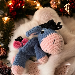 Könnte beinhalten: Ein gehäkeltes blaues und rosa Esel-Plüschtier mit schwarzem Garn für Mähne und Schwanz. Das Spielzeug liegt auf einer weißen, flauschigen Oberfläche.