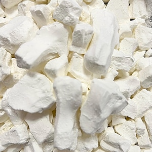 May include: A close-up of a bowl filled with white, irregularly shaped pieces of dried coconut.