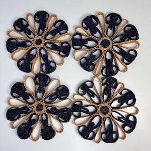 May include: Four decorative coasters with a floral design. Each coaster features a navy blue center and accents, with natural tan and white woven details. The coasters are arranged in a square formation, showcasing their intricate patterns.