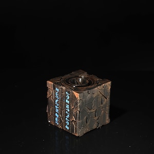 May include: A dark brown, cube-shaped object with a textured surface and a circular design on the top. The cube has the words "JUMPSTART" and "JUMPSTART" written on the sides in blue.