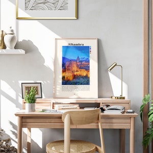 Puede incluir: Una impresi&oacute;n enmarcada de una pintura de acuarela del palacio de la Alhambra en Granada, Espa&ntilde;a. La impresi&oacute;n est&aacute; colgada en una pared blanca sobre un escritorio de madera con una l&aacute;mpara, libros y una planta en maceta.