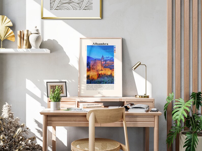 Puede incluir: Una impresi&oacute;n enmarcada de una pintura de acuarela del palacio de la Alhambra en Granada, Espa&ntilde;a. La impresi&oacute;n est&aacute; colgada en una pared blanca sobre un escritorio de madera con una l&aacute;mpara, libros y una planta en maceta.