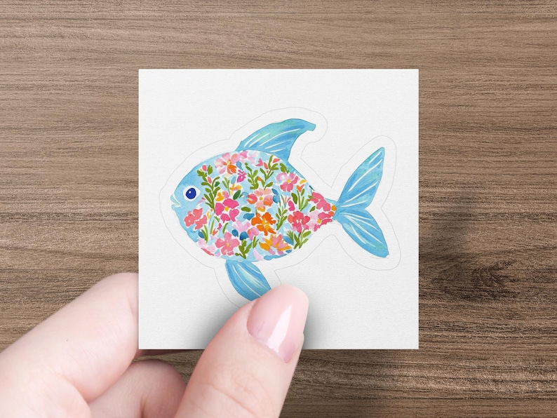 Sticker of a fish filled with colorful watercolor flowers, held by a hand.