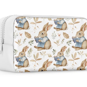 May include: White zippered makeup bag with a repeating pattern of brown rabbits holding blue books and brown leaves on a white background.